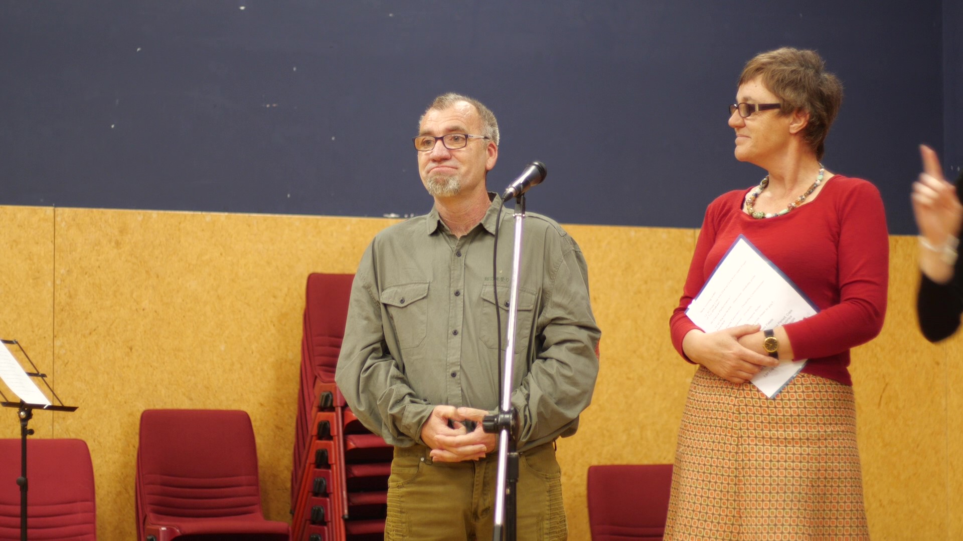 Disability activist and wearable arts creator, Paul Holmes at the Disability Pride Week celebration at Te Whaea – National Dance and Drama Centre, Wellington, December 2018. Paul is standing in front of the audience. Beside him is a microphone on a stand. He is about to speak about his wearable arts piece, ‘Disabled Oompah Loompah’ and disability pride. DPW volunteer, Bernadette Macartney, who MC’d the event is standing beside Paul. Disability activist and wearable arts creator, Paul Holmes at the Disability Pride Week celebration at Te Whaea – National Dance and Drama Centre, Wellington, December 2018. Paul is standing in front of the audience. Beside him is a microphone on a stand. He is about to speak about his wearable arts piece, ‘Disabled Oompah Loompah’ and disability pride. DPW volunteer, Bernadette Macartney, who MC’d the event is standing beside Paul.